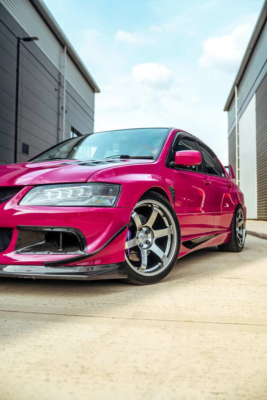 Magenta Lancer Evolution parked between two industrial units under a blue sky