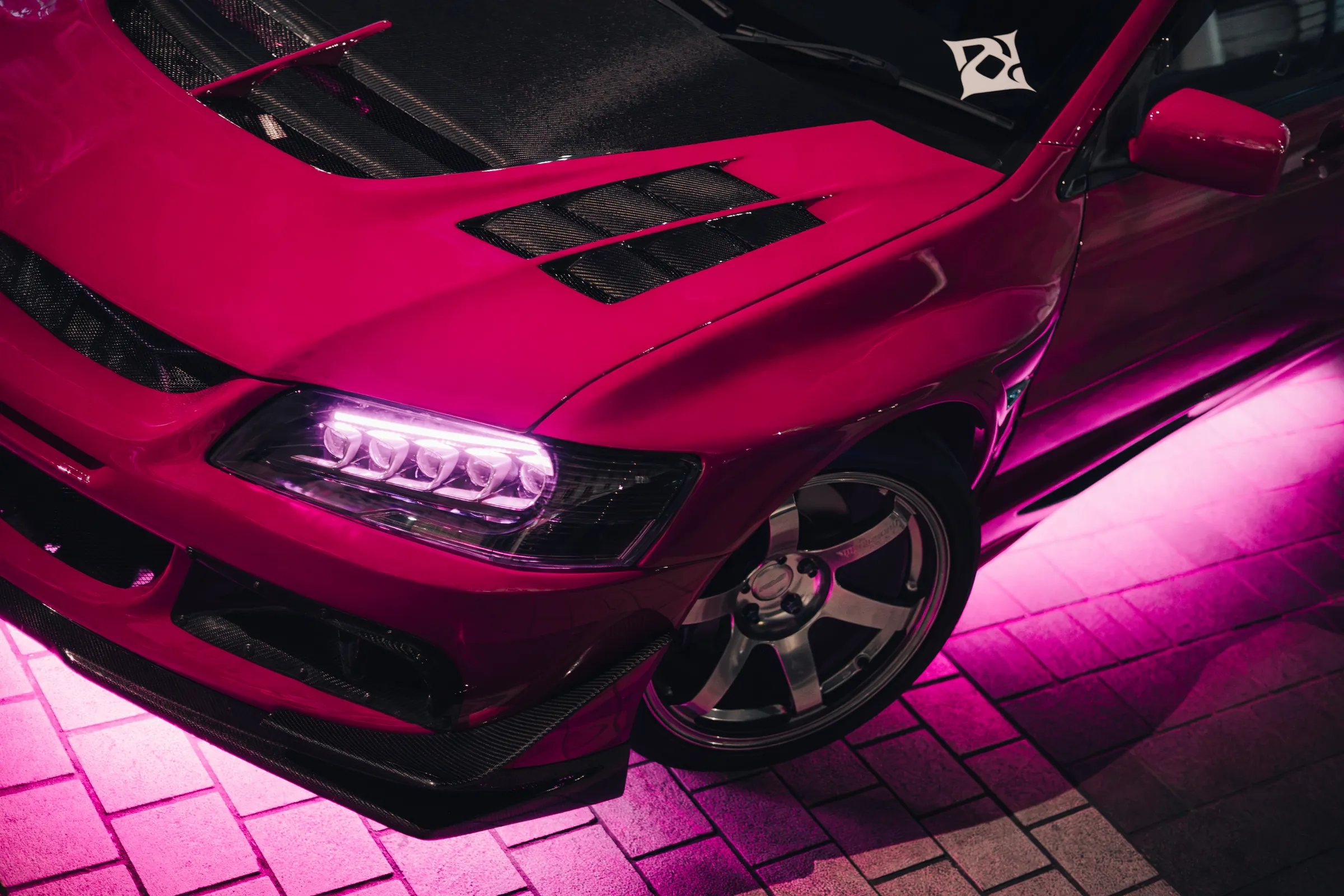 Magenta Lancer Evolution under pink underglow on the cobbles, the Dream Owners Club emblem on its windscreen