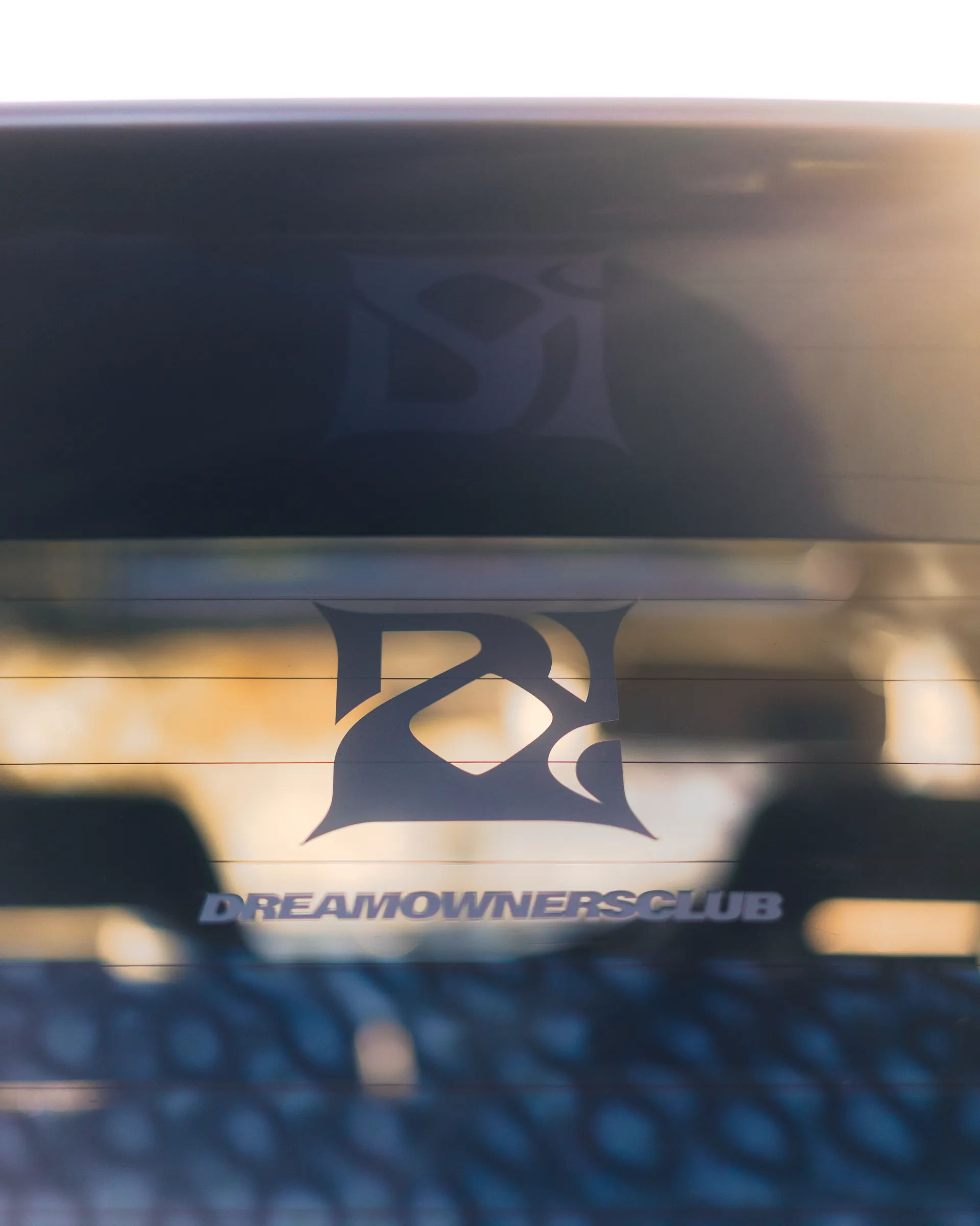 Dream Owners Club emblem decal on a rear window in warm light